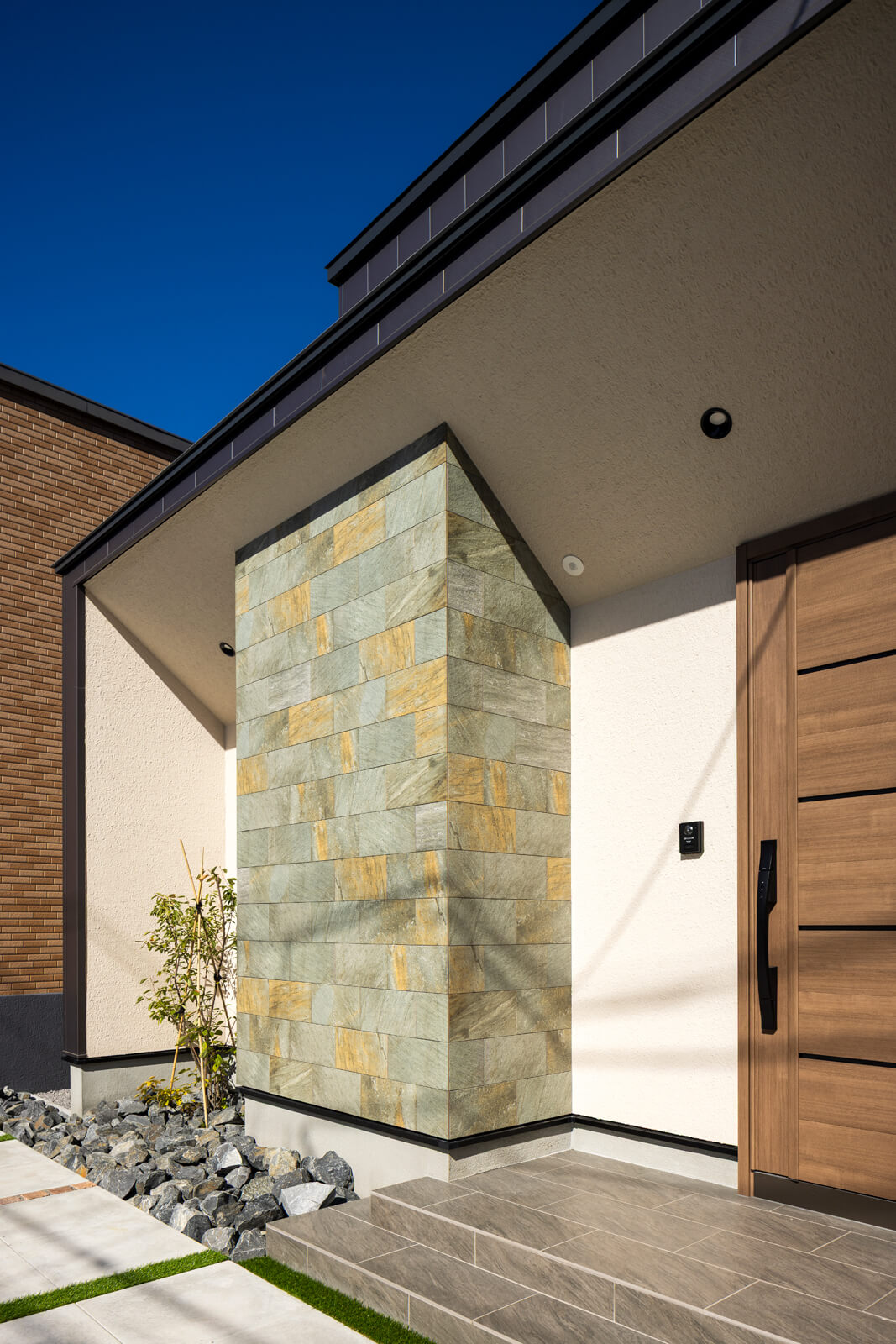 金属系サイディングとタイル、ジョリパッドの塗り壁を用いた質感あふれる外観。斜めの天井が広がりを感じさせる