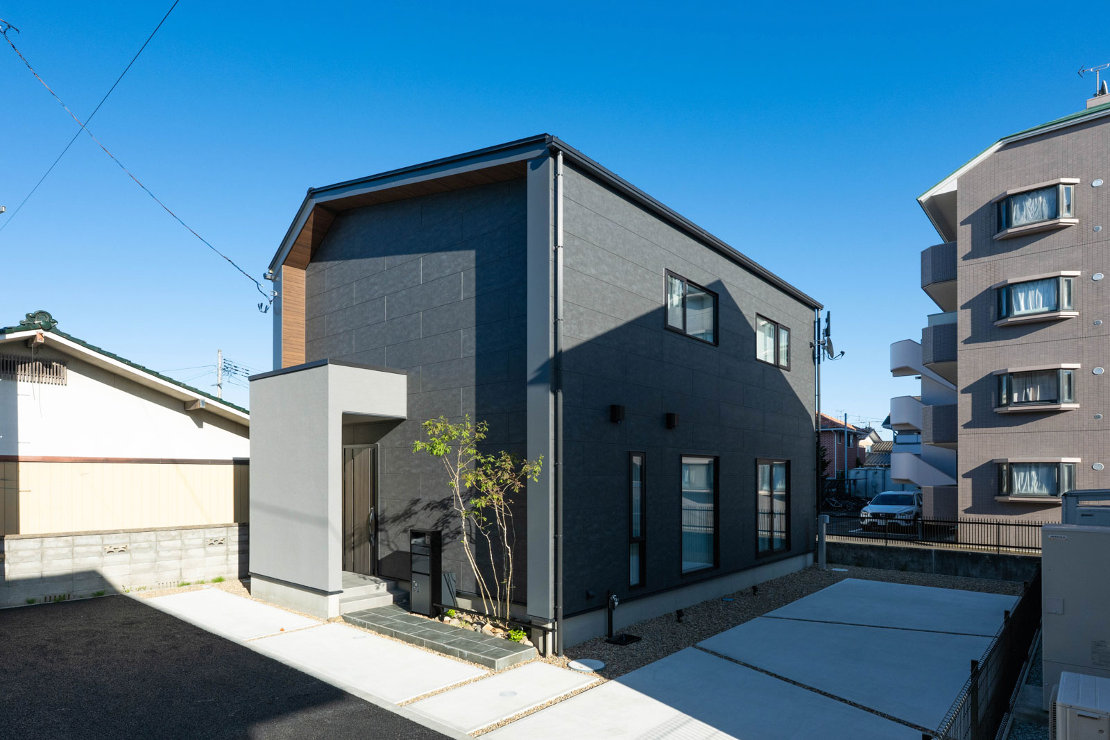 黒に近いグレーのサイディングが品格を感じさせる外観。ポイントに用いた塗り壁や木目調サイディングがアクセントを添えている。西側玄関のこの住まい。西陽とプライバシー対策のため、西側には窓を一つも設置しておらず、ファサードもすっきり
