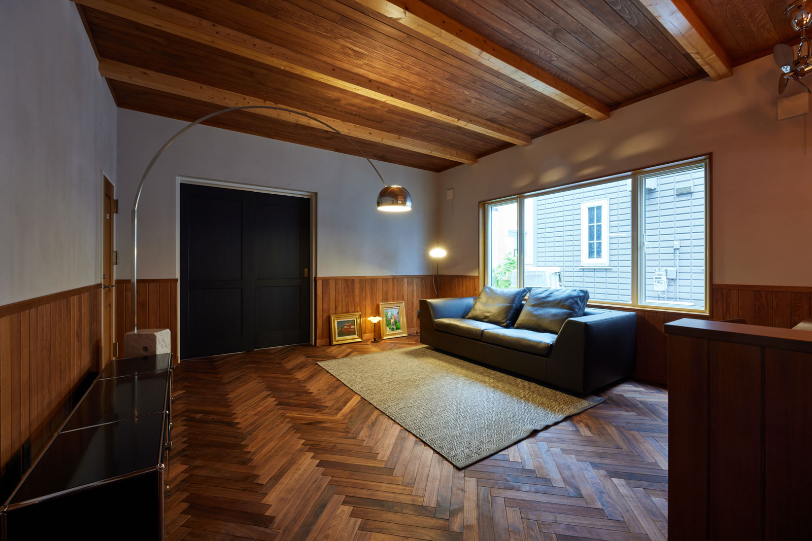 Mさんの一番の希望だったヘリボーンの床が存在感抜群のLDKは約18帖。ブラックウォールナットの無垢床と青森県産ヒバ材の腰板、梁、天井板に、グレーがかった土佐漆喰の塗り壁が調和している。引き戸の奥は寝室