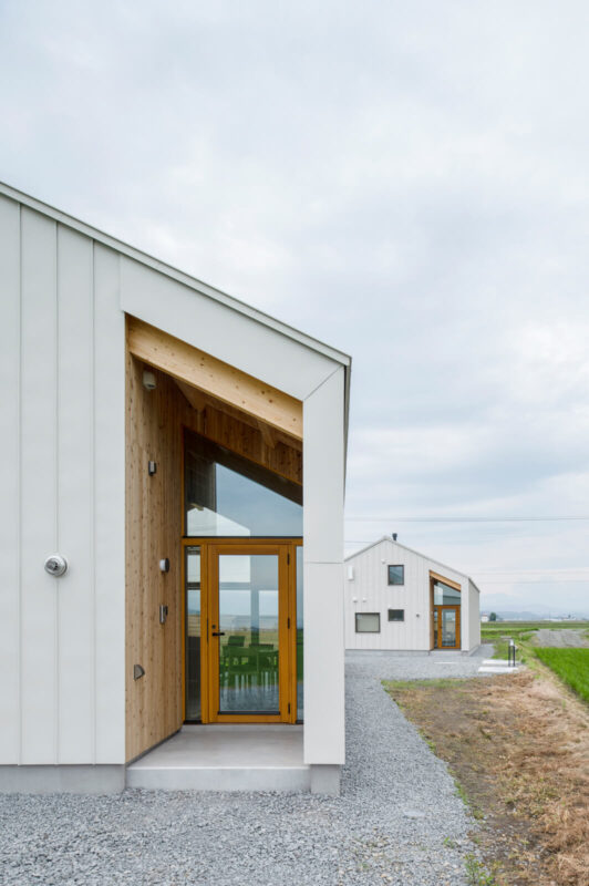 勾配に沿った鋭角のデザインが目を引く玄関ポーチ。ドアを含む開口をガラス張りにすることで、田園の緑の地平線や美しい夕陽を室内へと呼び込む