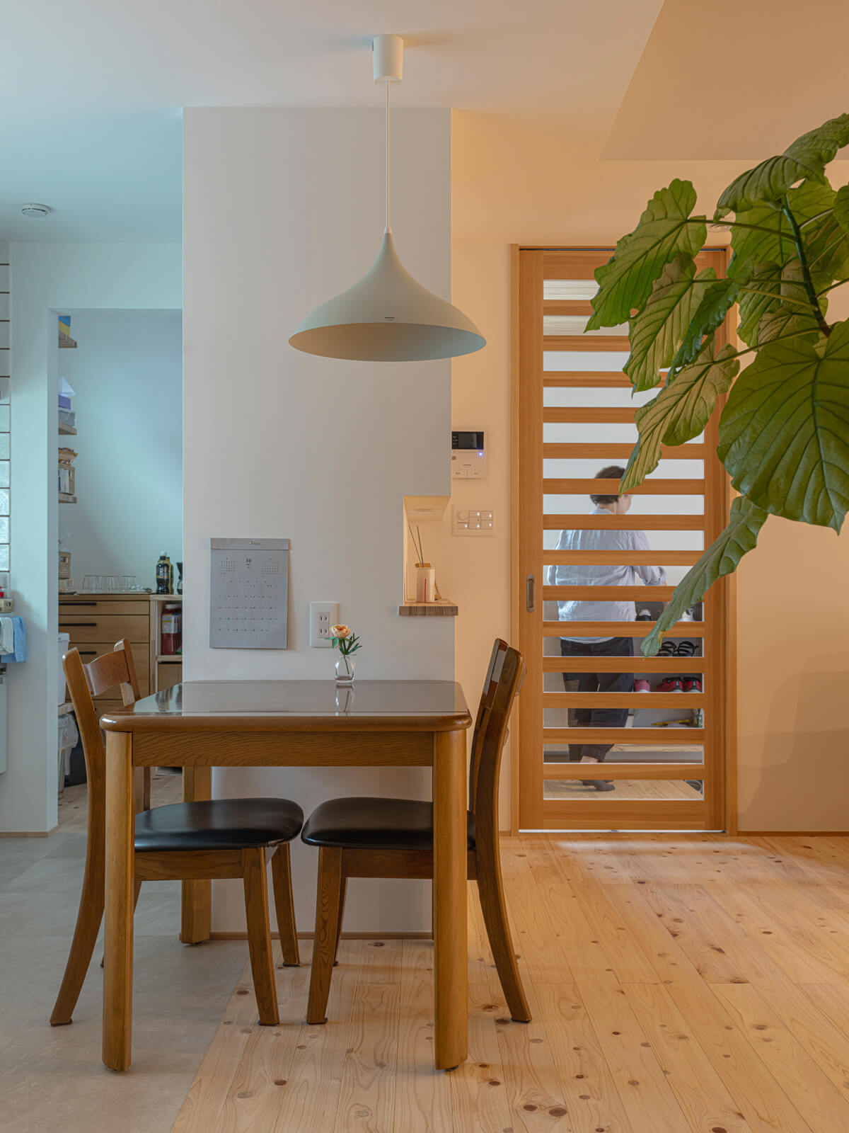 二人暮らしなので、ダイニングはコンパクトに。床材は豊かな香りと節の風合いが魅力のヒノキの無垢床。右手の横桟をあしらった引き戸の先が玄関