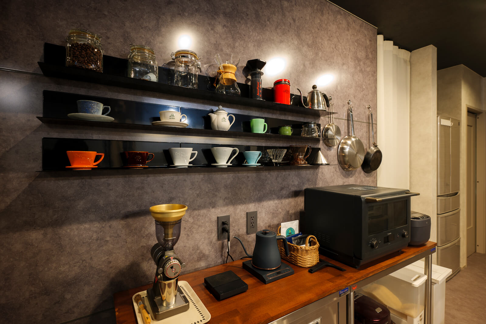 木製の天板はご夫妻がホームセンターで購入し塗装したそう。カップが飾られている棚やフライパンを吊るすフックはマグネットで壁に付けている