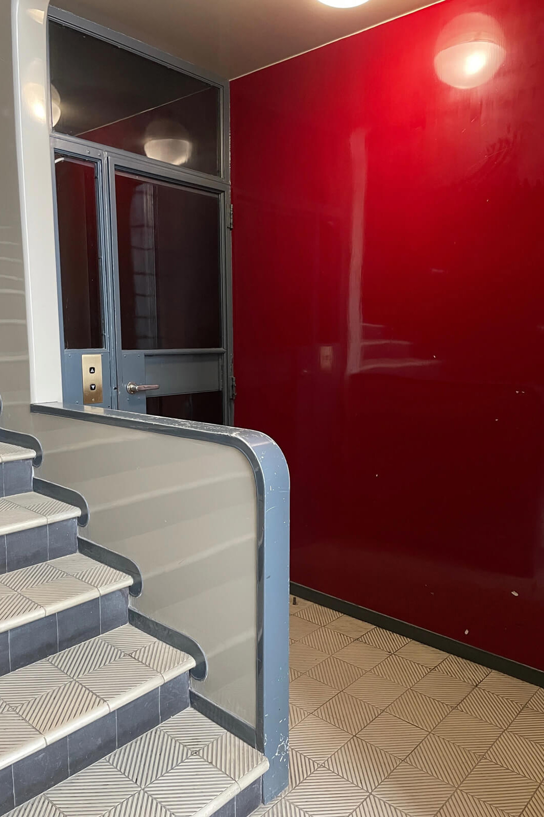 曲線的な階段とエレベーターホールの色合い、素材感が時代を感じさせる