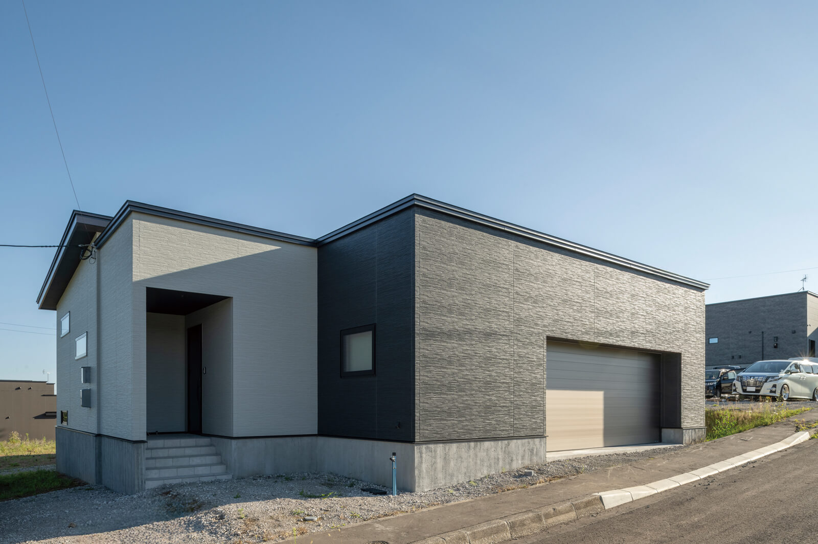 モノトーンのツートーンカラーで仕上げたシックな外観。大きなガレージは、夜は間接照明で印象的に照らされる