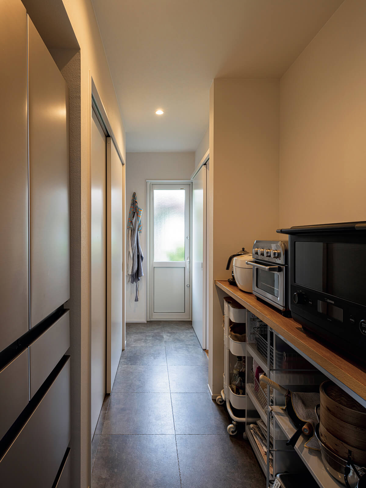 大容量のパントリーは収納の機能に加え、勝手口や洗面スペースへ通じる回遊動線の一部を兼ねている。壁面収納は扉付きで、ほこりっぽくなりにくく、見た目もすっきり