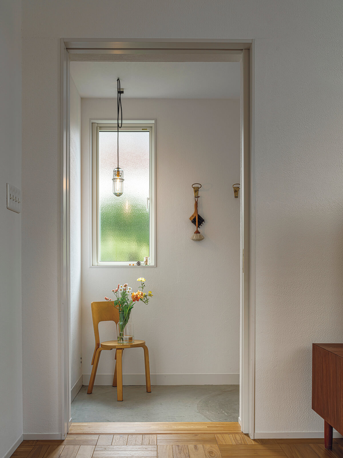 外の緑を抽象的に映す窓やPeter Ivy(ピーター・アイビー)のペンダントライト、季節の花と、その花台のビンテージチェア。住まいの余白が豊かさを感じさせる