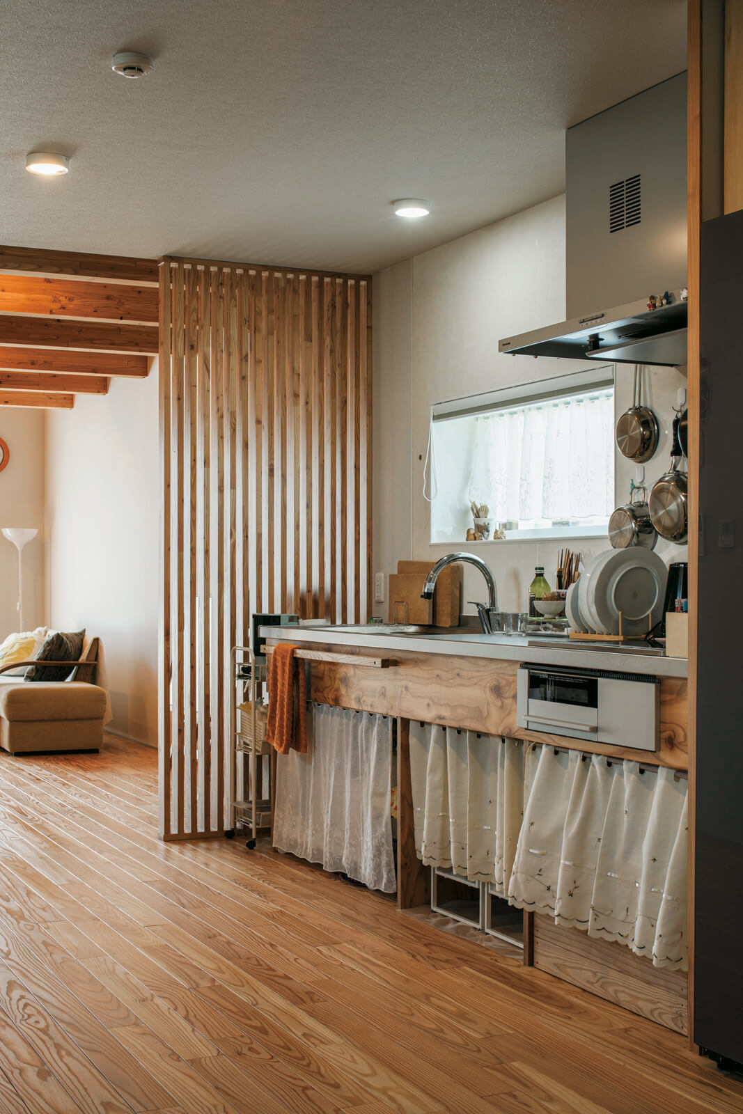 カラマツ合板を用いた造作キッチンはあらかじめ収納を設けずに、ご夫妻が使い勝手がいいように市販のラックを組み合わせた。キッチン横にはルーバーを設け、リビングとキッチンを緩やかに仕切っている