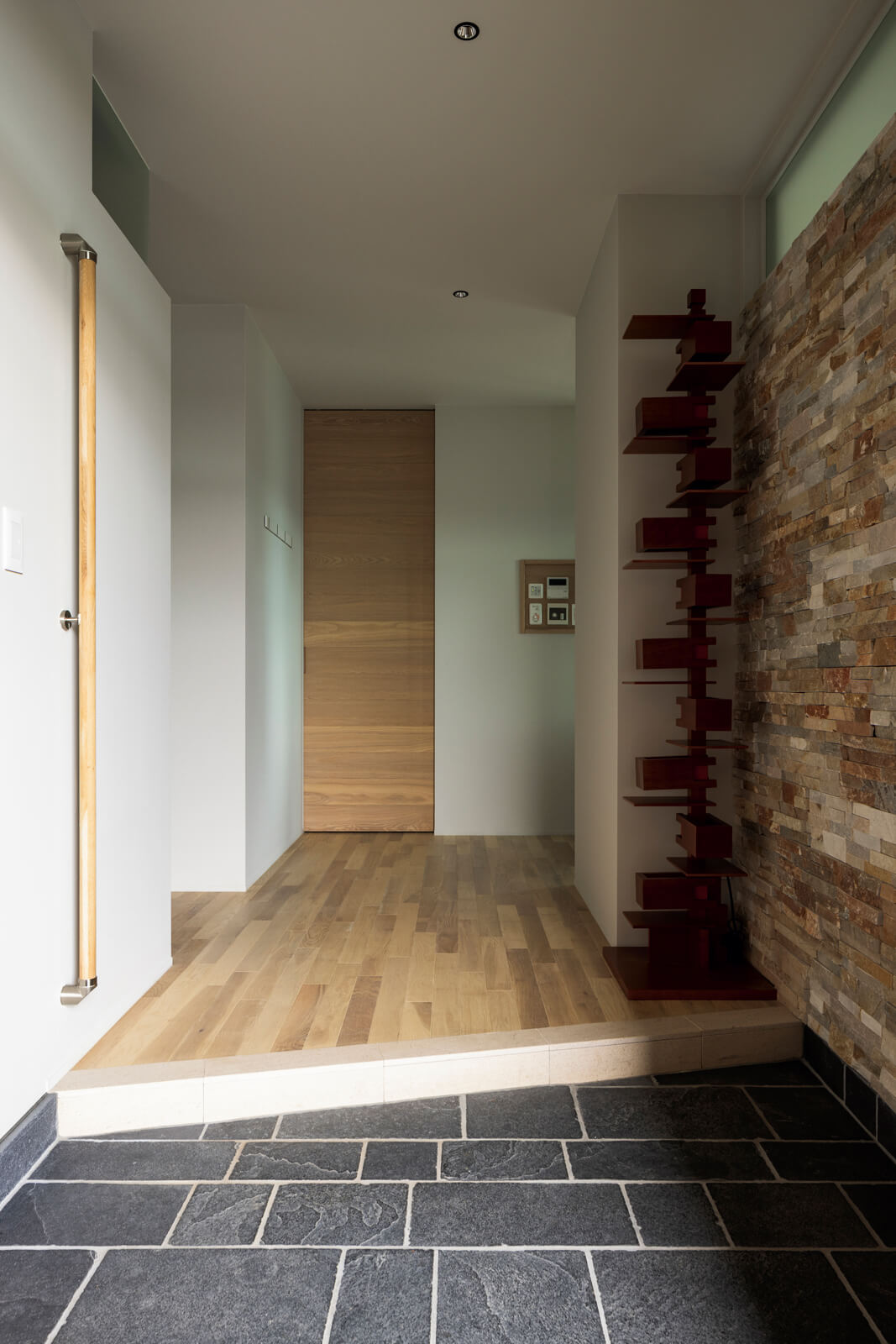 玄関の壁には、ポーチから回り込むように同素材の石材をランダムに凹凸をつけて張った。フランク・ロイド・ライトのフロアライトをつけると、光に浮かび上がる陰影が美しい