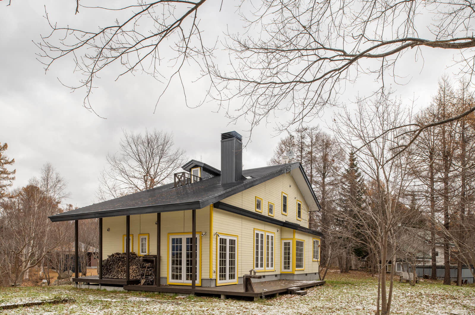 ご夫妻の「明るい色を」という要望で、淡い黄色のサイディングを用いた外観。建物に沿うようにウッドデッキを造作。土間の出入り口のあるデッキは薪置き場も兼ね、屋根の庇を延ばした