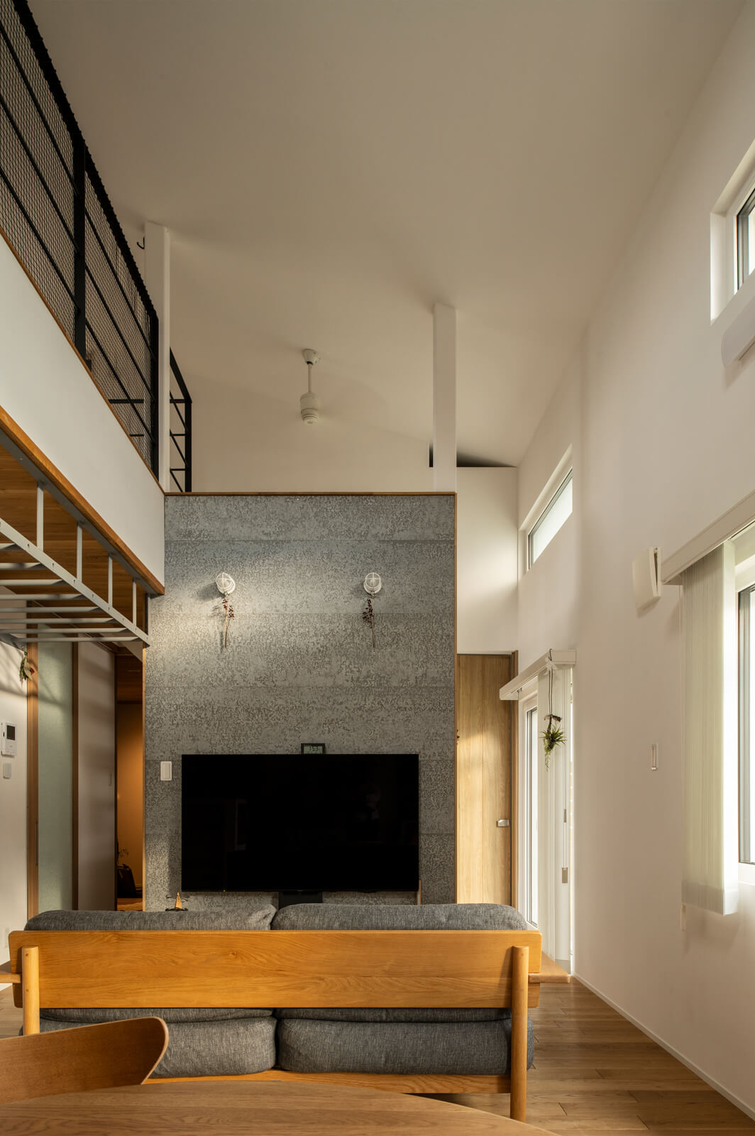 硬質なSOLIDOを張った壁とヤナギやケヤキの無垢材を用いたテレビ台収納も造作仕様。壁裏は階段で、右手奥に進むと階段下空間を生かした愛犬スペースと寝室がある