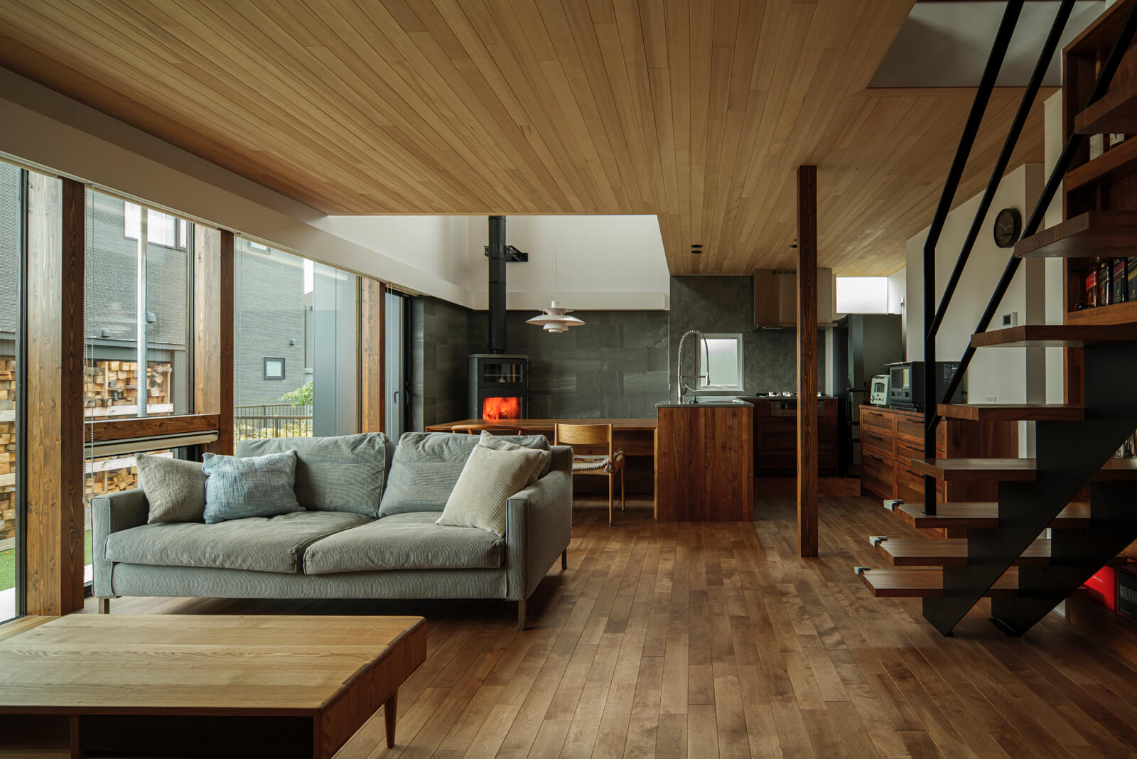 約21帖のLDK。南面は大部分が窓なので日光が入って明るい。床は無垢カバ材、天井は無垢ツガ材を使用。天井の色を床の色より明るくすることで、天井をより高く感じさせる効果がある