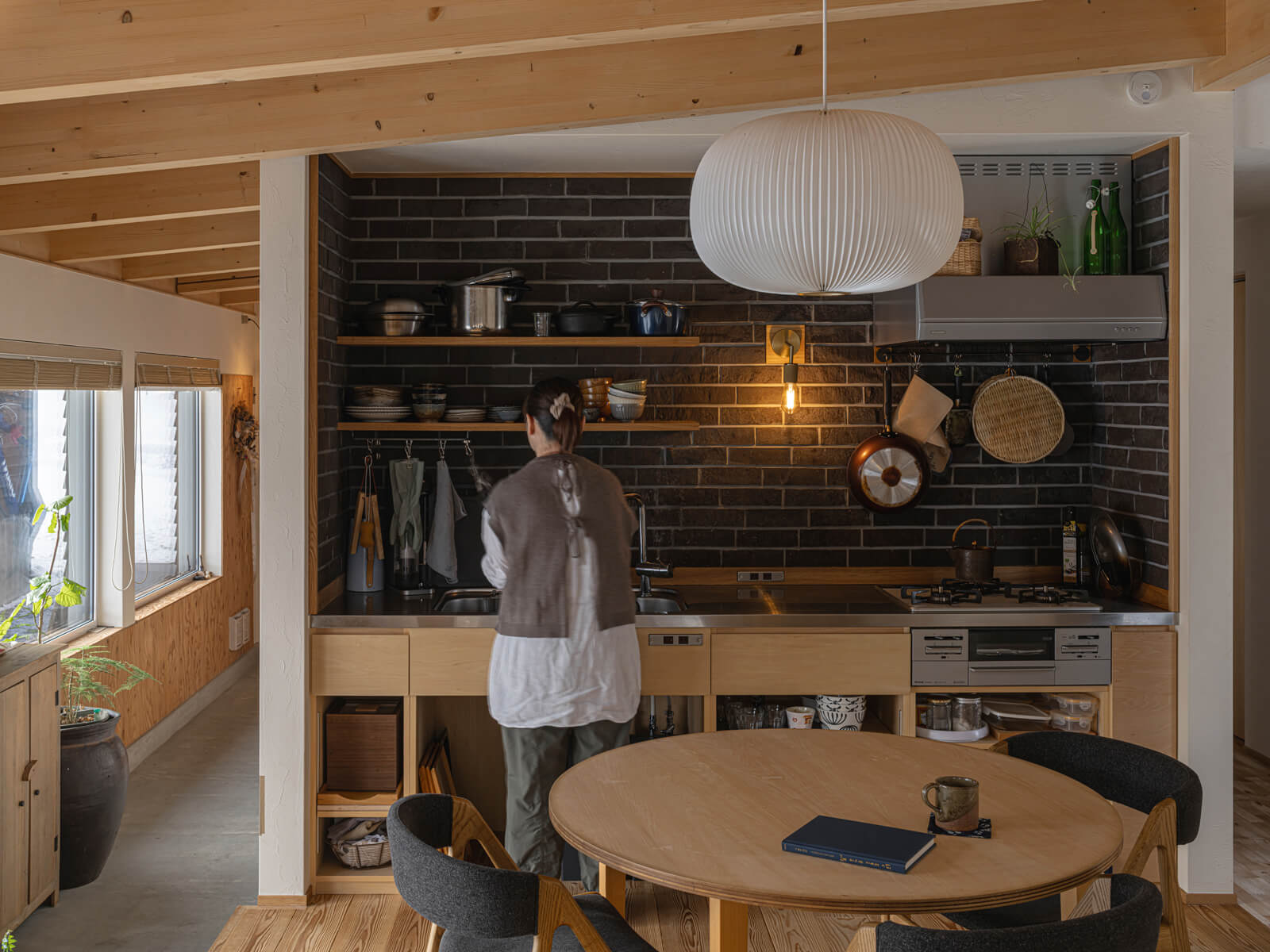 壁付けの造作キッチンは、壁面にシックな色合いが魅力の江別産のマンガンレンガを張り、シナベニアやタモ材を用いて仕上げた。ダイニングテーブルも、キッチンと合わせて大工が製作した