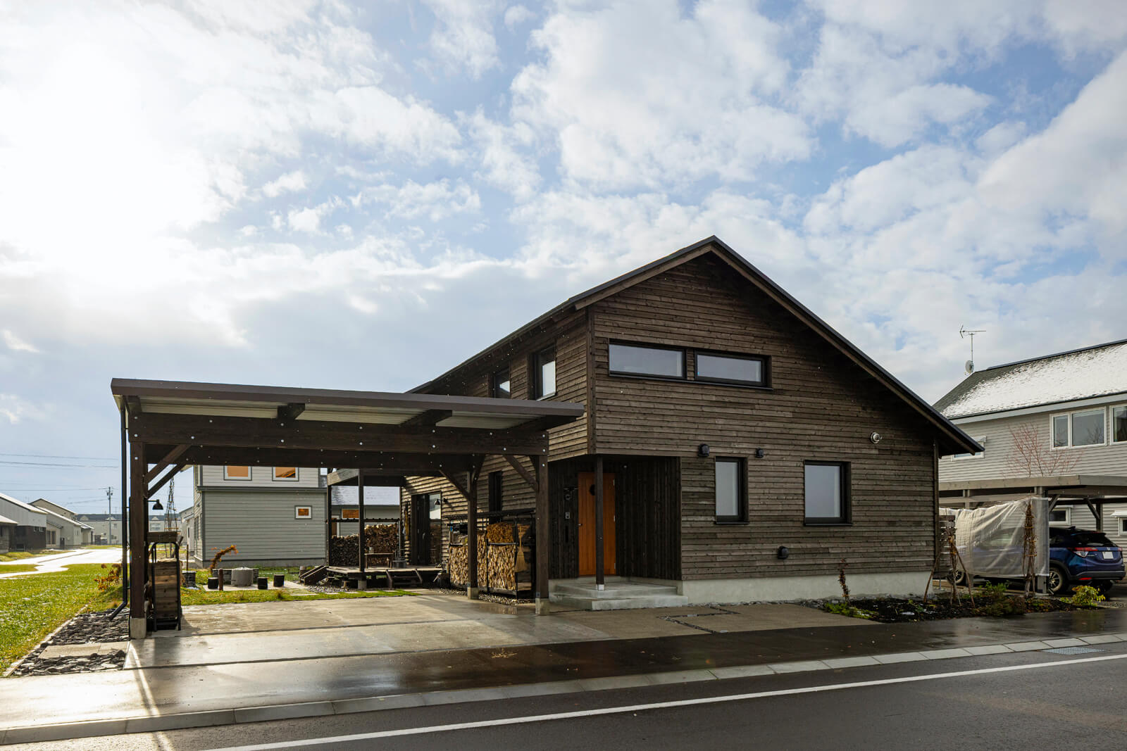 ウッドデッキまで覆う大きな三角屋根と横張りの道南スギの外観。ゆとりあるカーポートは、屋根のある屋外空間としても活躍
