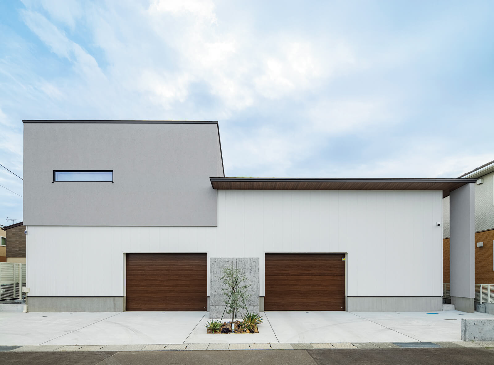 ホワイトのガルバリウム鋼板とグレーの塗り壁、木目調のシャッターなど、異なる素材や色合いが調和し、表情豊かなファサードになっている。屋根には約7kWの太陽光発電パネルを搭載