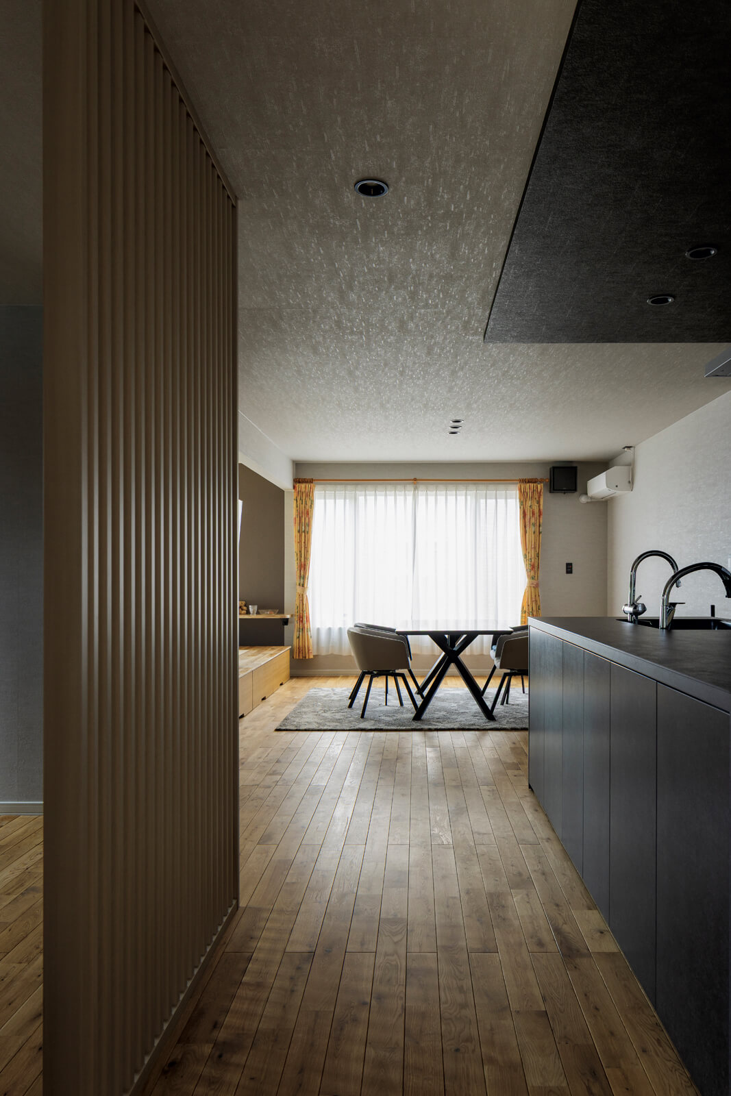 キッチンからダイニングを見る。目線の抜けの良さが広がり感を演出。キッチンの前には、来訪者の目線をさりげなく遮る木製のルーバーを設置した