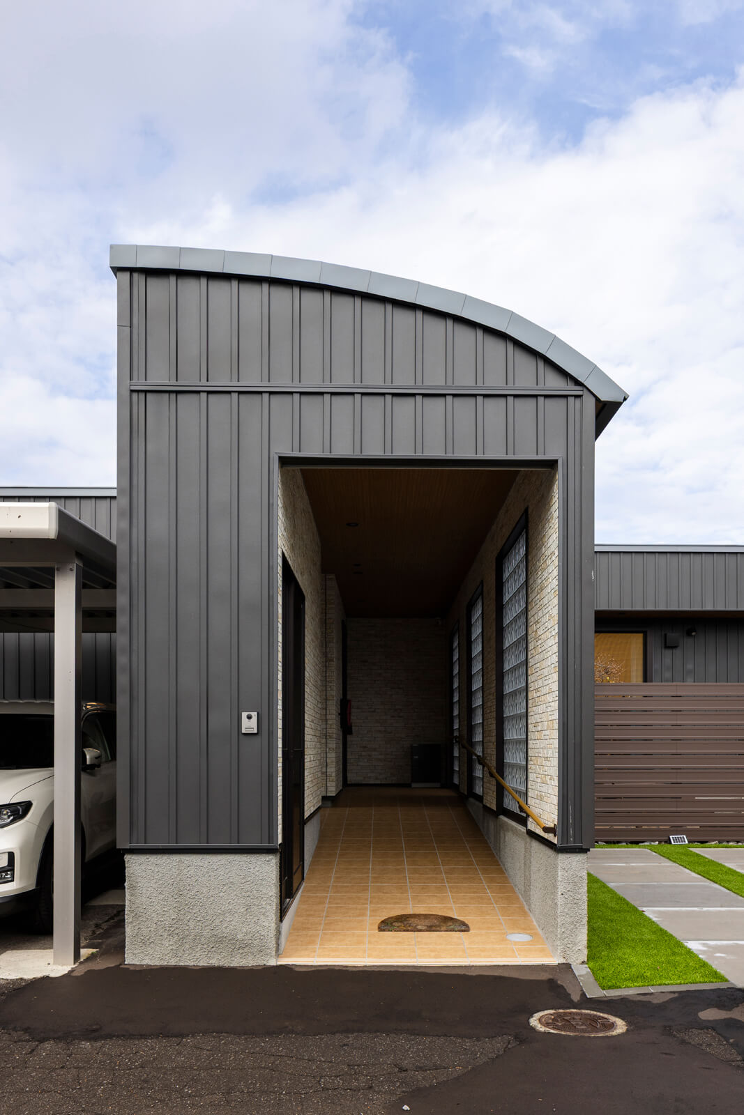 アールをつけた屋根と光を通すガラスブロックが印象的な玄関アプローチ。デザインは奥さんが気に入っていた旭川の菓子店の設えを参考にしたそう