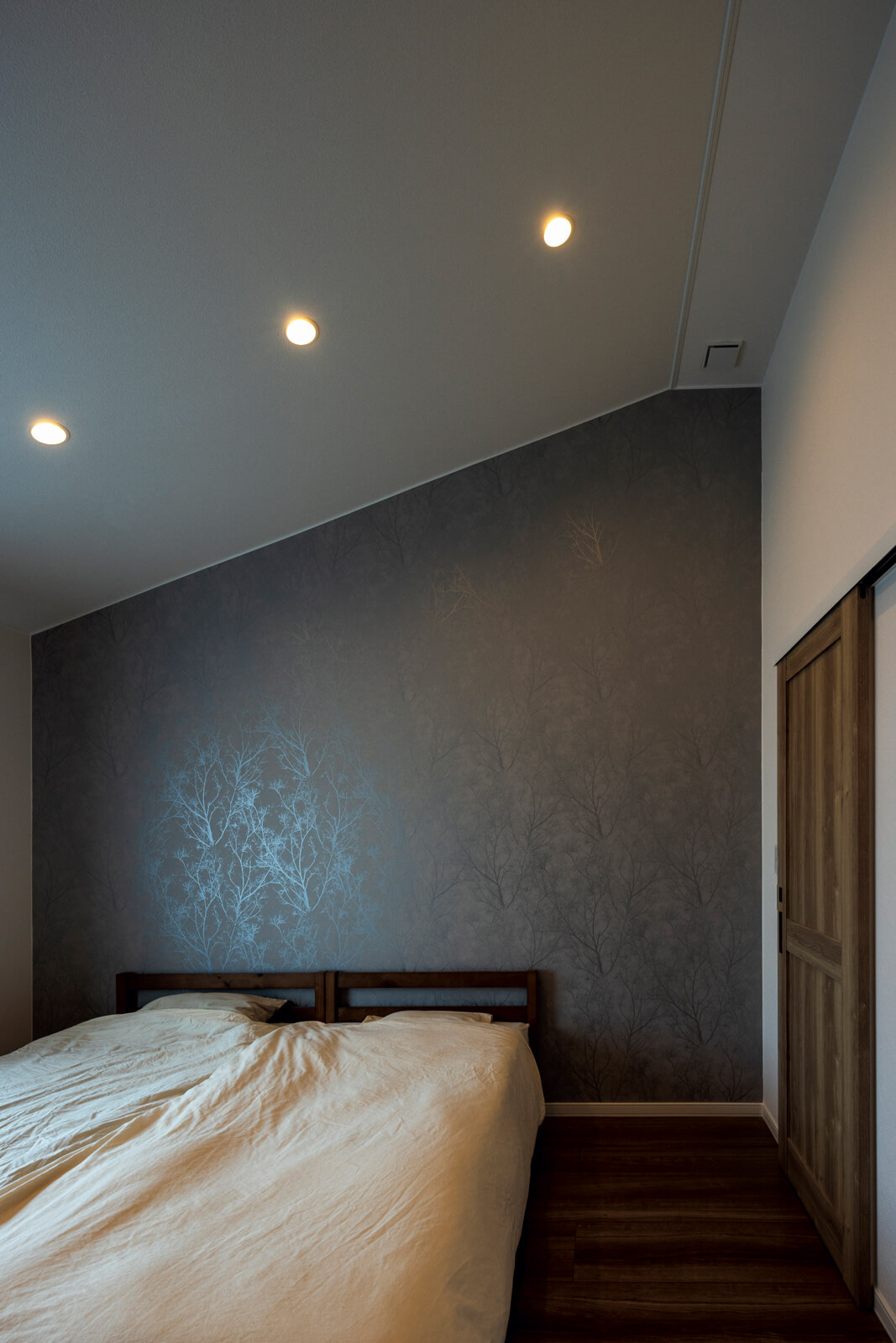 ウォークインクローゼットを併設した寝室は、屋根なり天井にダウンライト、濃色のアクセントクロスを採用し、落ち着いた雰囲気に