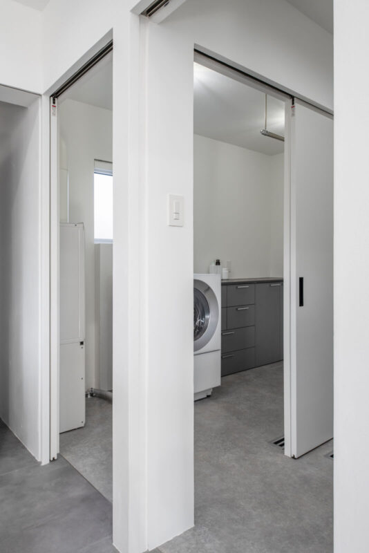 キッチンのすぐ隣が、ランドリールームと浴室・洗面脱衣室。洗面脱衣室からも直でアクセスできるランドリースペースは、洗う・乾かす・干すを1ヵ所で完結する。水まわりはご夫妻以外はほとんど使わないため、クロスやクッションフロアを採用してコストを調整した