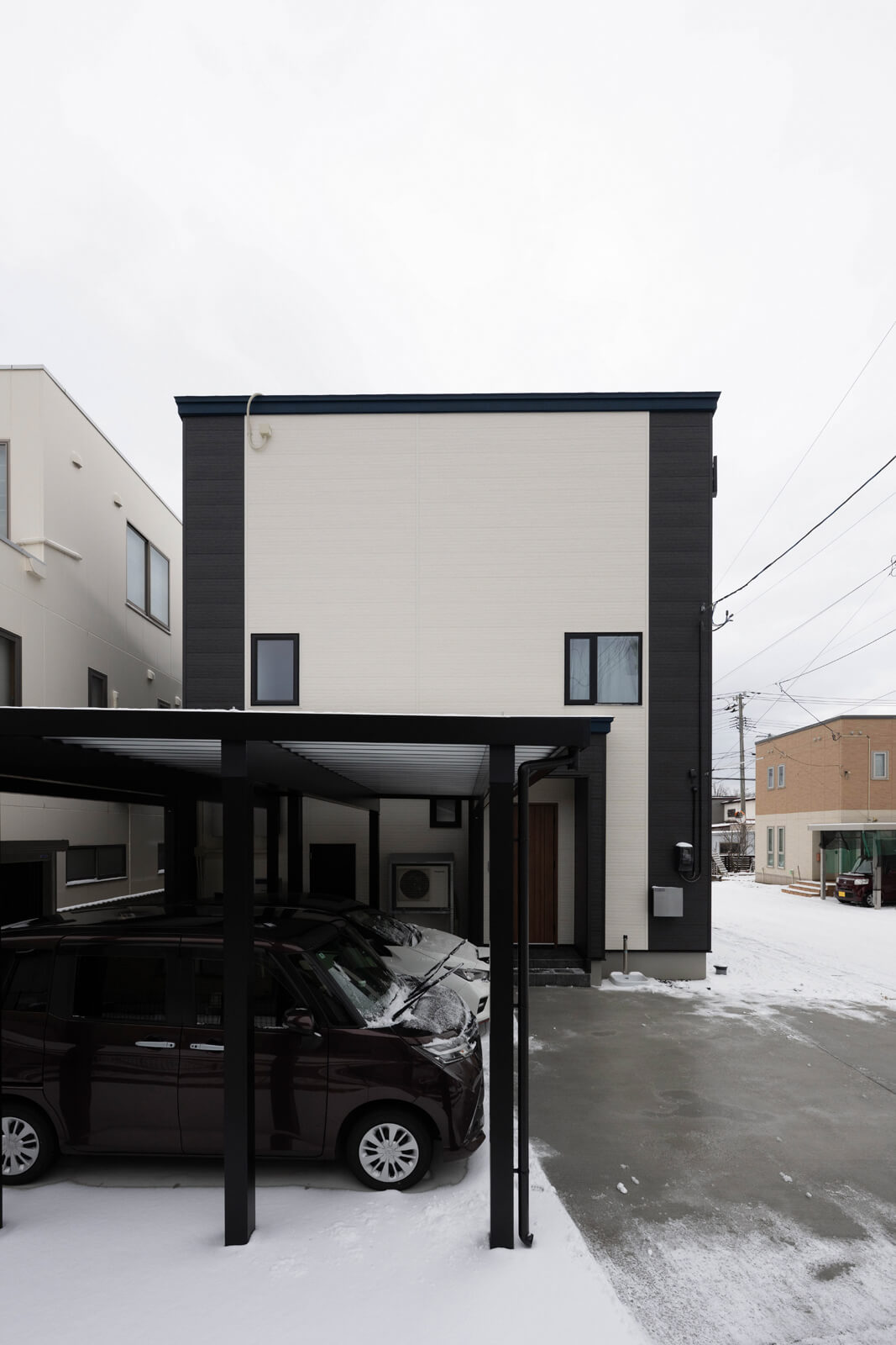 外壁材は黒とオフホワイトのガルバリウム鋼板。住まいには2つの非常口を設けていて、2階左側の窓はそのうちの1つ。階段の踊り場からカーポートの上に出られるように設計している