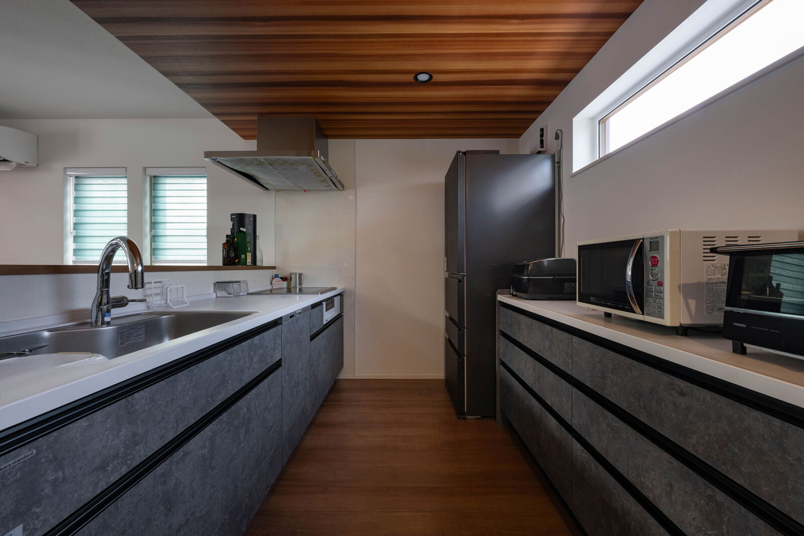 ハイサイドライトから安定した自然光が入り、北側でも明るいキッチン。グレーのキッチンと木目の天井はリビングとデザインを合わせた