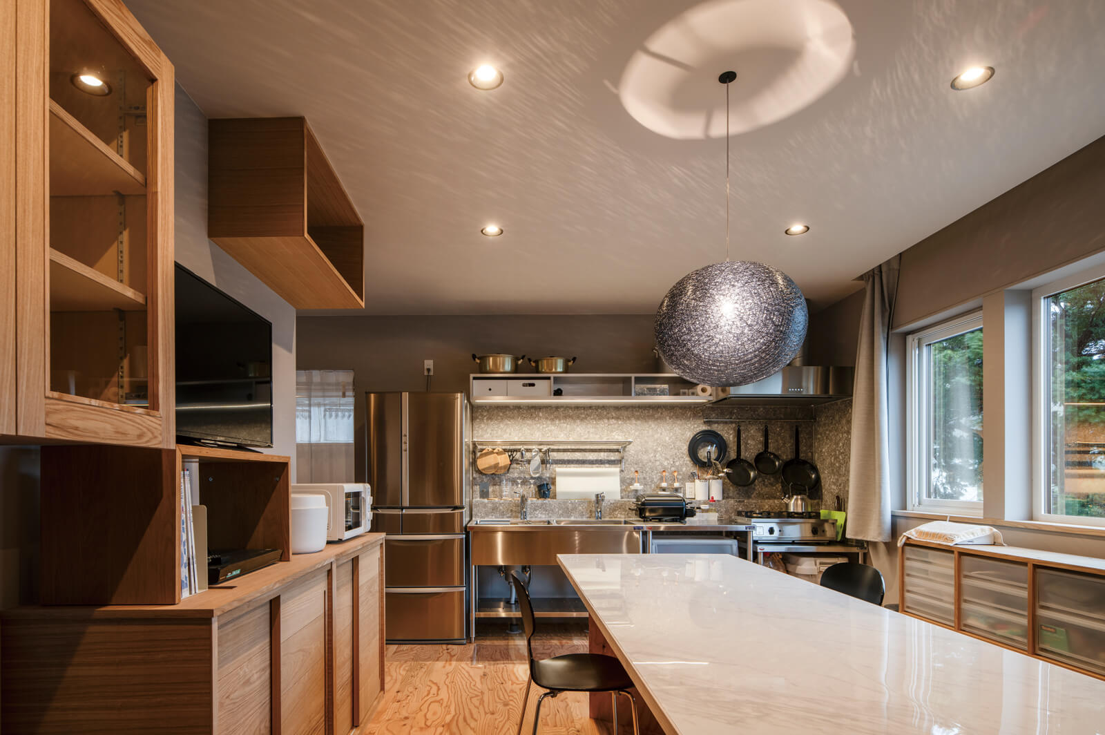 ミニマルな空間でステンレスと木、タイルが心地よいハーモニーを奏でるダイニング・キッチン。繊細な陰影が奥行きのある表情を与えるペンダント照明は、Aさんのお気に入り