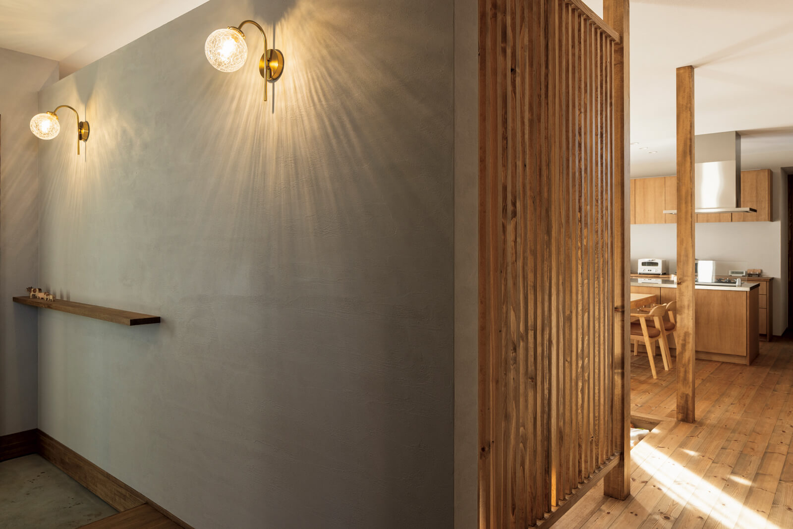 玄関ホールの壁には、漆喰壁に美しい陰影を描く壁付け照明を設置。リビングの薪ストーブの熱が玄関ホールにも伝わるよう、漆喰壁の上部にはスリットを入れ、ルーバーの間仕切りを採用した
