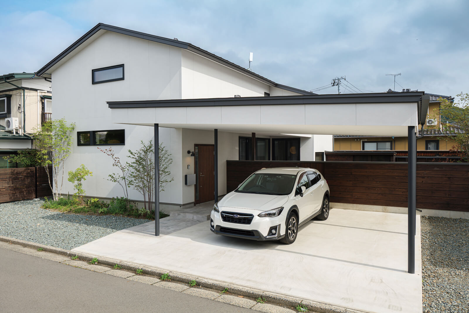 切妻屋根の住宅とシンプルなデザインのガレージに低い木塀を組み合わせ、全体として落ち着いた雰囲気の外観に