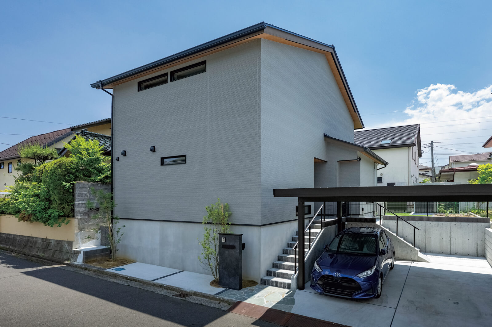 切妻屋根が印象的な外観。家は北側の道路に面していて、2台分の屋根付きカーポートも完備。玄関へは、道路側から直接向かう階段と、ガレージ側からつながる階段の2つを設けて利便性を高めた